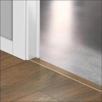 Light brown wooden floor trim with quickstep classic incizo profile used as multi-use profile by white door frame and metal wall
