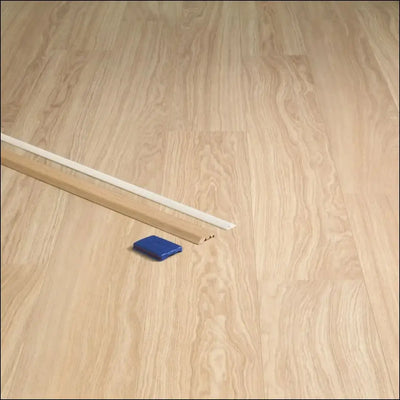 Light wood quickstep classic incizo profile baseboard with white top edge and blue plastic multi-use profile tool nearby