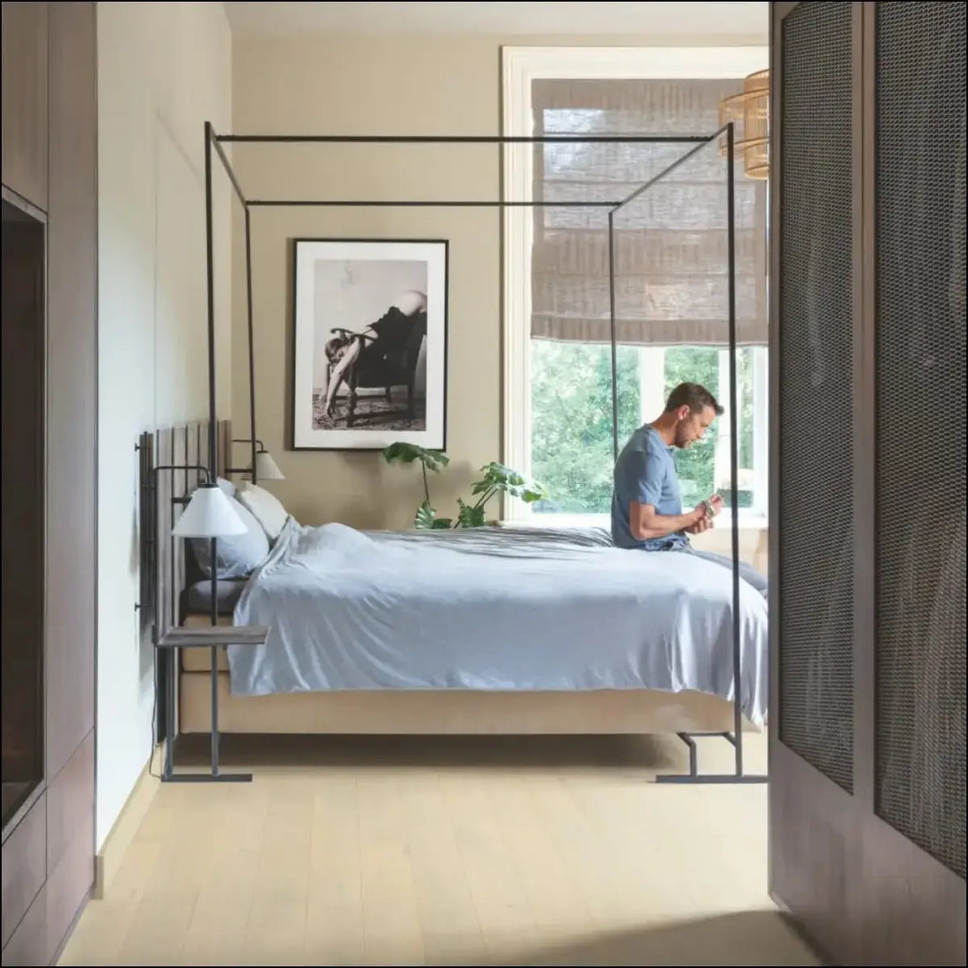 Black metal four-poster bed frame with slender legs featured alongside quick-step amato wintry forest oak extra matt flooring