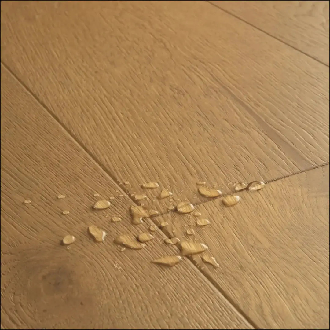 A cluster of translucent water droplets on a light brown quick-step cala dark chestnut oak extra matt wooden floor