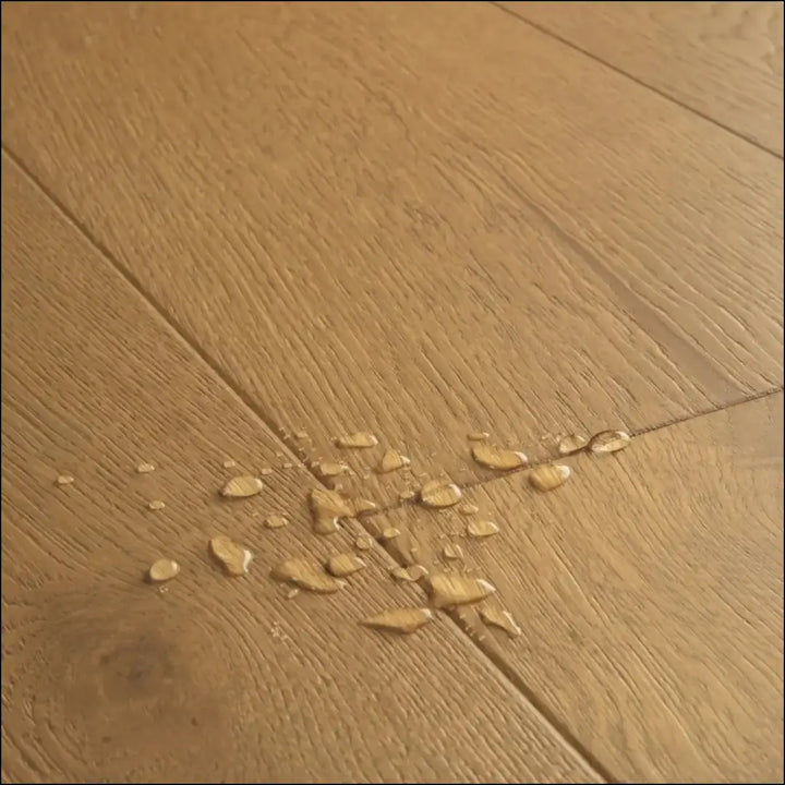 A cluster of translucent water droplets on a light brown quick-step cala dark chestnut oak extra matt wooden floor