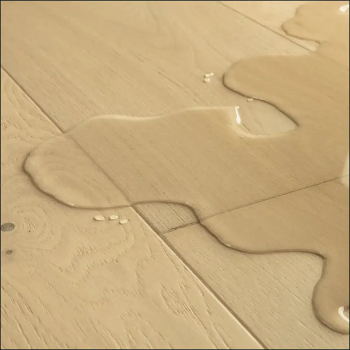 A shallow translucent puddle on quick-step cala pearl white oak extra matt floor showing white oak extra texture