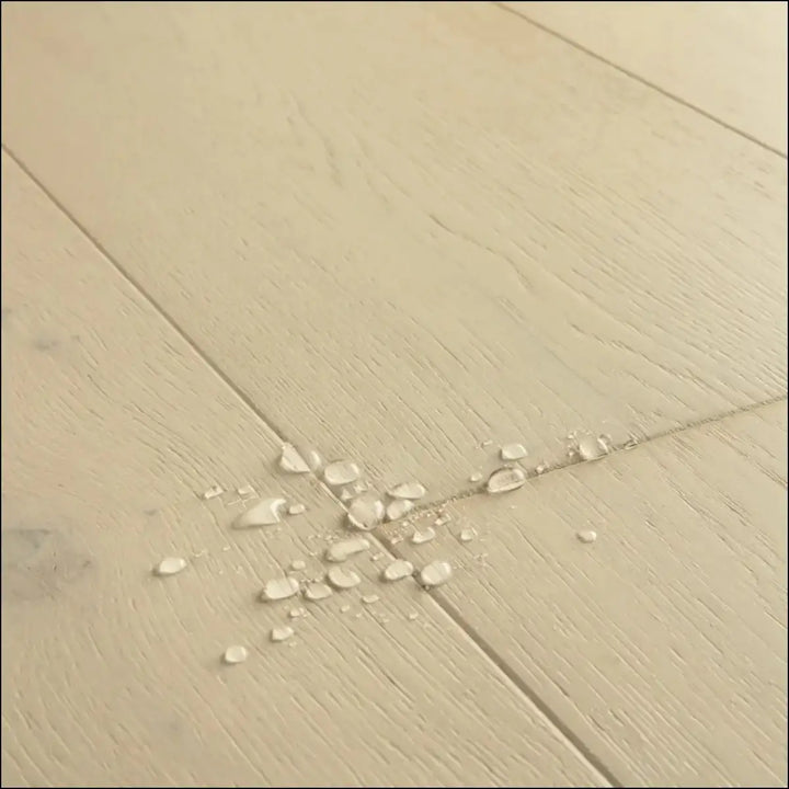 Beige wood-plank flooring with subtle grain and water droplets in quick-step cala wintry forest oak extra matt finish