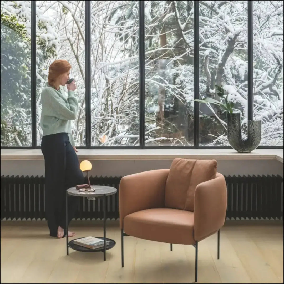 Warm terracotta upholstered armchair with sleek black metal legs beside quick-step cala wintry forest oak flooring