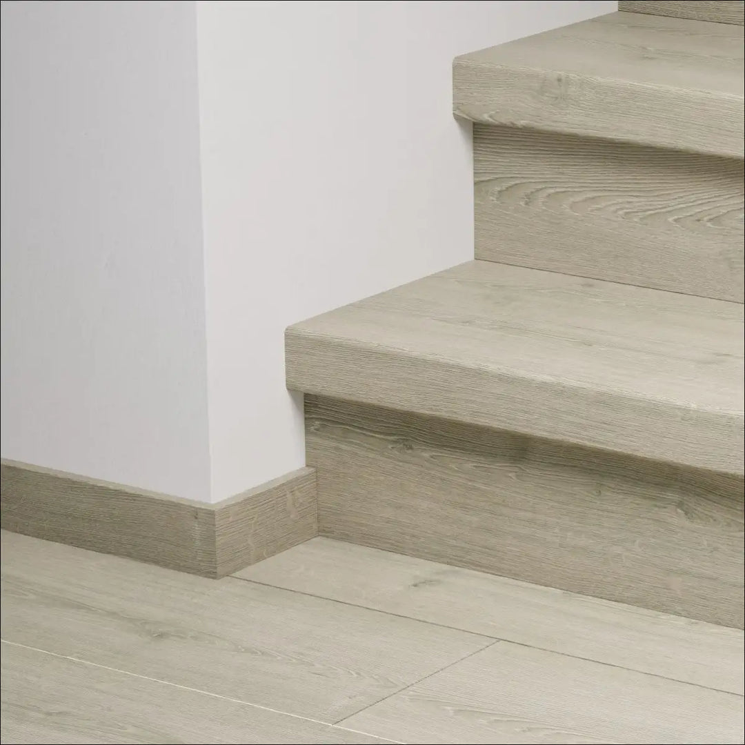 Modern light gray wooden quick-step capture stair cover with visible grain texture and matching baseboard stair nosing