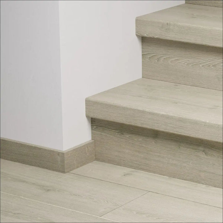 Modern light gray wooden quick-step capture stair cover with visible grain texture and matching baseboard stair nosing