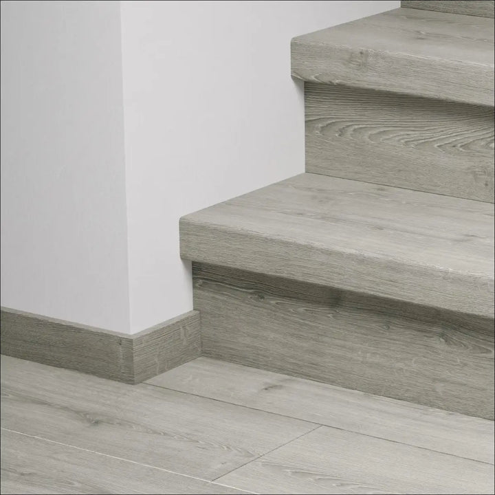 Gray wood-grain quick step capture stair cover with matching floor and baseboard featuring stair nosing detail
