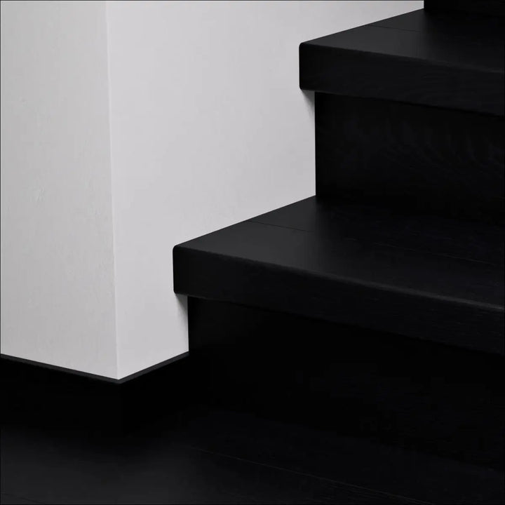 Black quick-step capture stair covers with minimalist floating steps and stair nosing against white wall