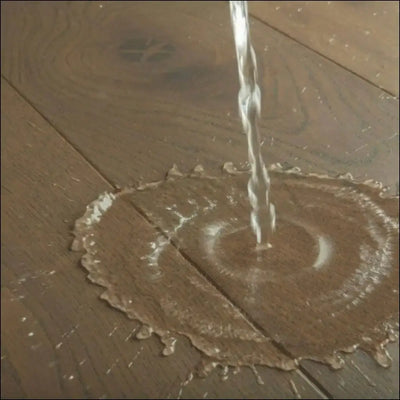 A clear stream of water pours onto a quick step cascada brown vintage oak extra matt wood floor