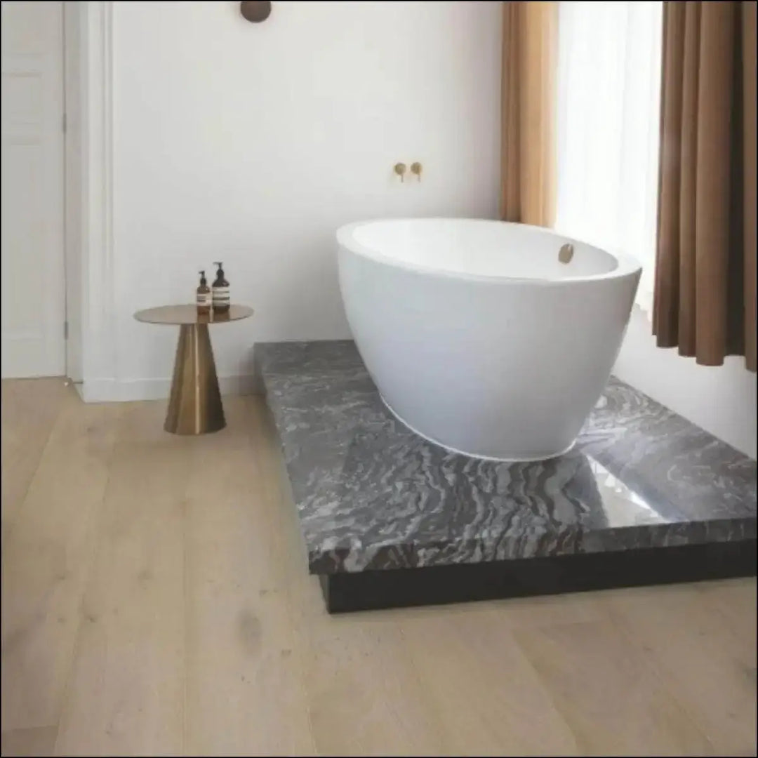 White freestanding bathtub with oval design on dark gray marble platform with quick step cascada oak extra matt flooring