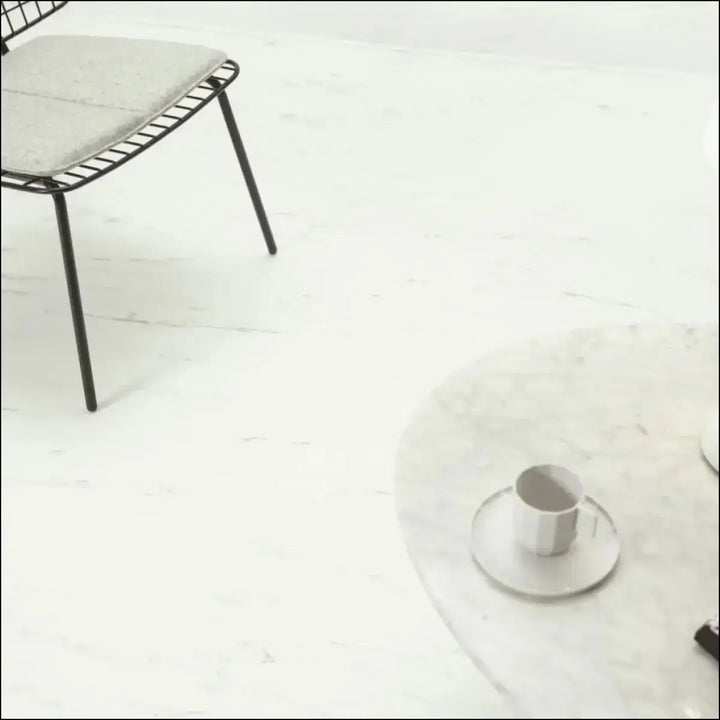 A minimalist white ceramic coffee cup on a marble table showcasing quick-step oro vinyl tile white marble carrara avstu40231