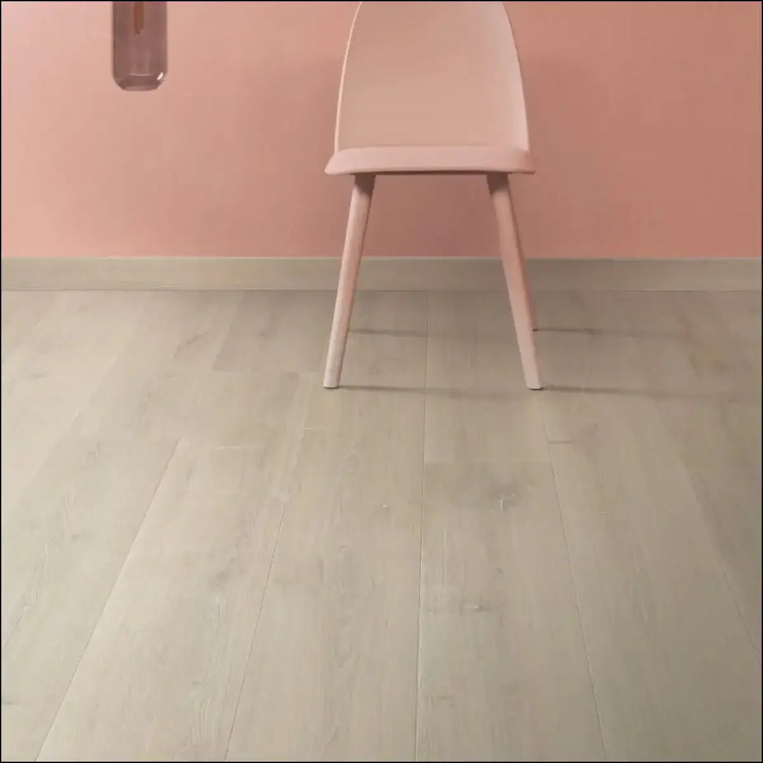 A minimalist pink plastic chair with slender legs paired with quick-step capture brushed oak beige laminate flooring