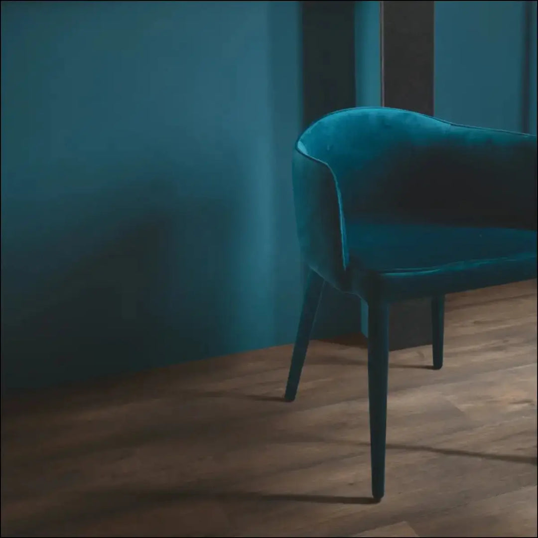 A sleek teal velvet armchair with dark legs shown on quickstep capture waxed oak brown laminate flooring