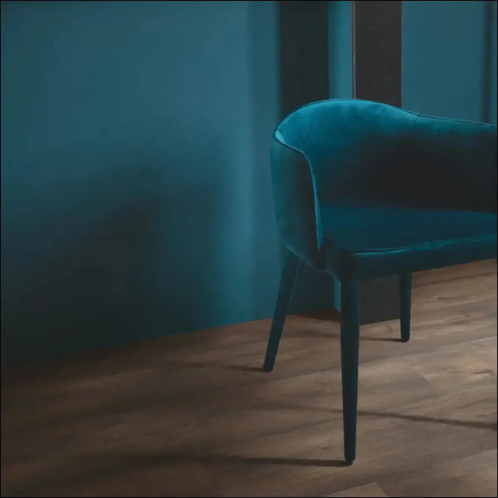 A sleek teal velvet armchair with dark legs shown on quickstep capture waxed oak brown laminate flooring