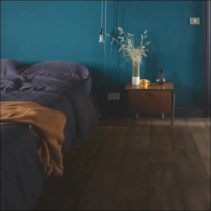 A tall glass vase with dried grasses on a wooden nightstand on quick-step capture waxed oak brown laminate flooring