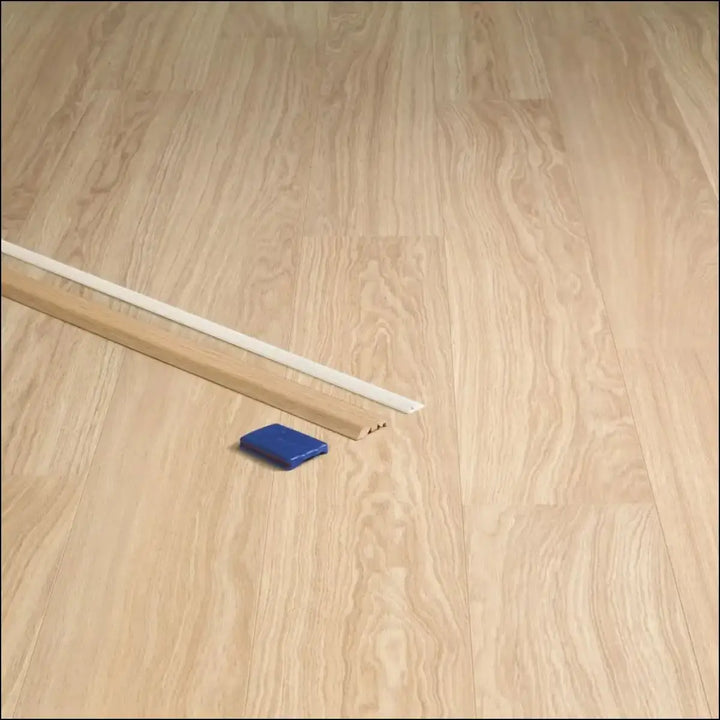 Light wood quickstep classic incizo profile baseboard with white top edge and blue plastic multi-use profile tool nearby