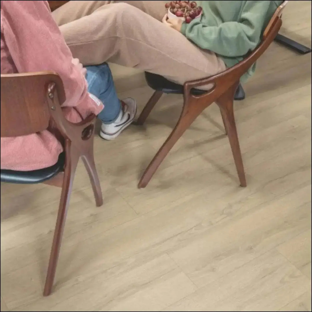 A sleek mid-century modern wooden chair with curved back and tapered legs on quickstep classic laminate sandy greige oak flooring