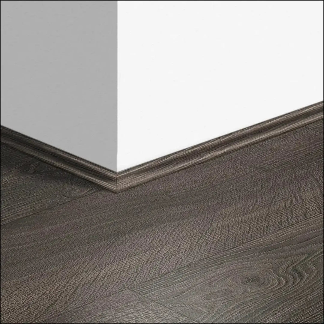 Dark gray wood grain quickstep classic scotia baseboard with subtle texture seamlessly joins white wall and matching floor