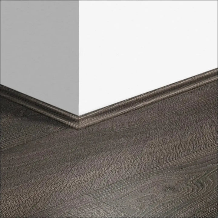 Dark gray wood grain quickstep classic scotia baseboard with subtle texture seamlessly joins white wall and matching floor