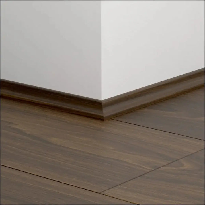 Dark brown wooden quickstep classic scotia beading baseboard with smooth finish along white walls and dark flooring