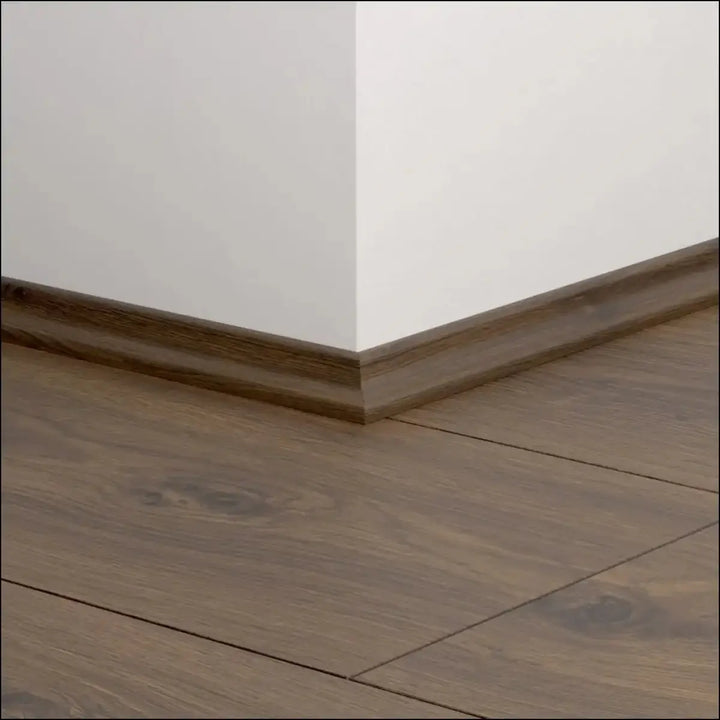 Dark brown wooden quickstep classic scotia beading with a smooth finish along the white wall and wood floor corner