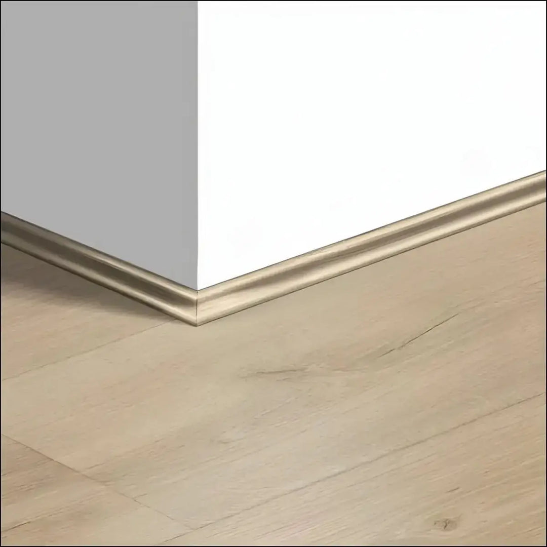 Gold-toned sleek metal baseboard trim from quickstep majestic scotia along light gray and white walls with beige wood-look floor
